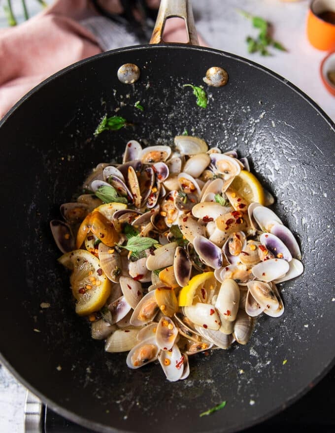 Almejas completamente cocidas en una sartén con láminas de limón, escamas de ajo y chile, todas las almejas se han abierto, cocinadas y listas para hacer pasta de almejas 