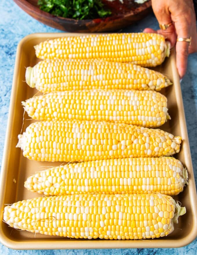 Ingredients to make the mexican street corn salad with lots of fresh seasonal corn, and the dressing in another bowl, and the chopped ingredients 