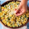 A hand holding a chips and scooping some mexican corn salad with creamy cilantro lime dressing, jalapenos and avocados