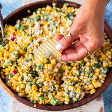 A hand holding a chips and scooping some mexican corn salad with creamy cilantro lime dressing, jalapenos and avocados