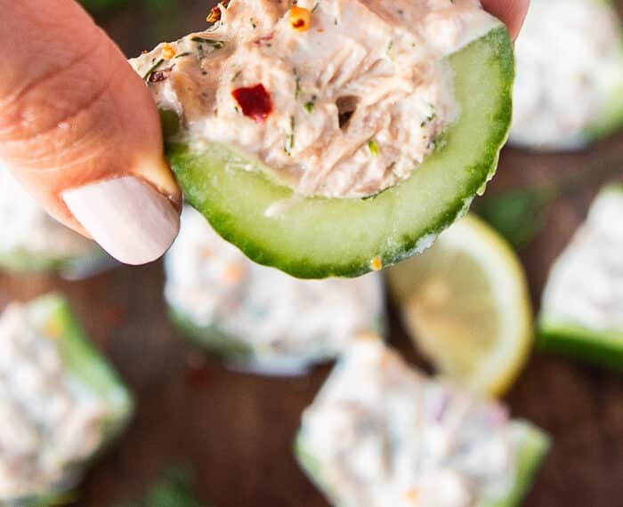 A hand holding a piece of cucumber topped with tuna salad for the best bites of tuna cucumber salad