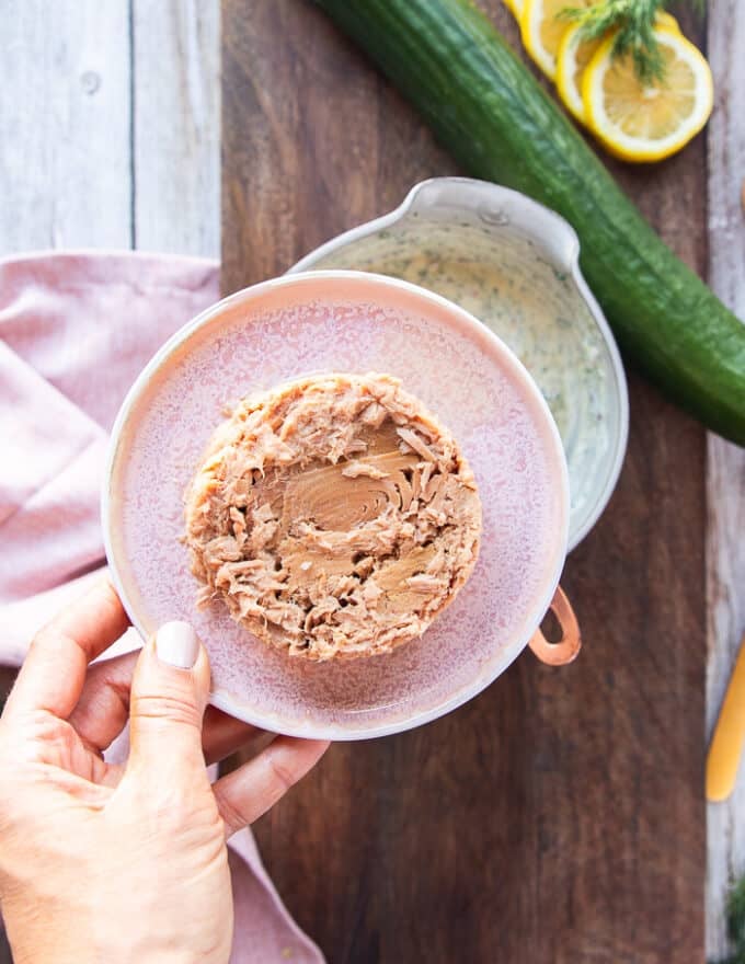 drained canned tuna in a plate and a hand holding it 