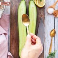 a hand holding a spoon and scooping the flesh from the sliced cucumbers
