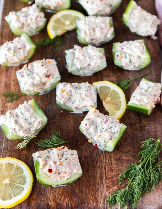 tuna and cucumber salad on a wooden board surrounded by dill and lemon slices.