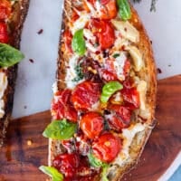 one whole caprese toast close up showing the sourdough toast, the ripe sweet baby tomatoes, mozzarella, garlic, basil leaves and chilli flakes drizzled with olive oil