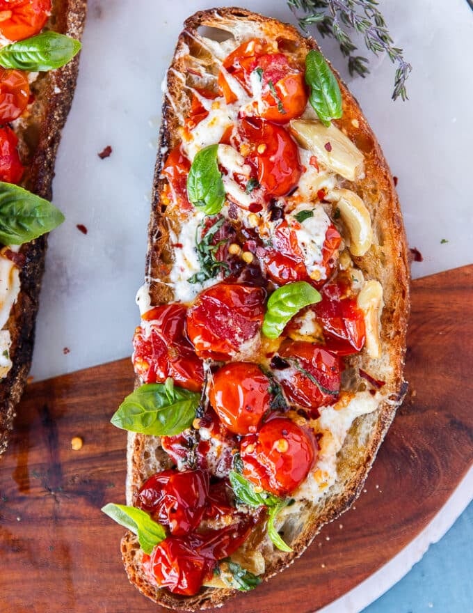 one whole caprese toast close up showing the sourdough toast, the ripe sweet baby tomatoes, mozzarella, garlic, basil leaves and chilli flakes drizzled with olive oil 
