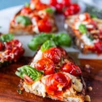 close up of a cut up caprese toast showing the blistered tomatoes, mozzarella and basil leaves drizzled with some olive oil and light balsamic syrup
