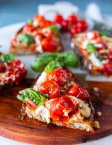 close up of a cut up caprese toast showing the blistered tomatoes, mozzarella and basil leaves drizzled with some olive oil and light balsamic syrup