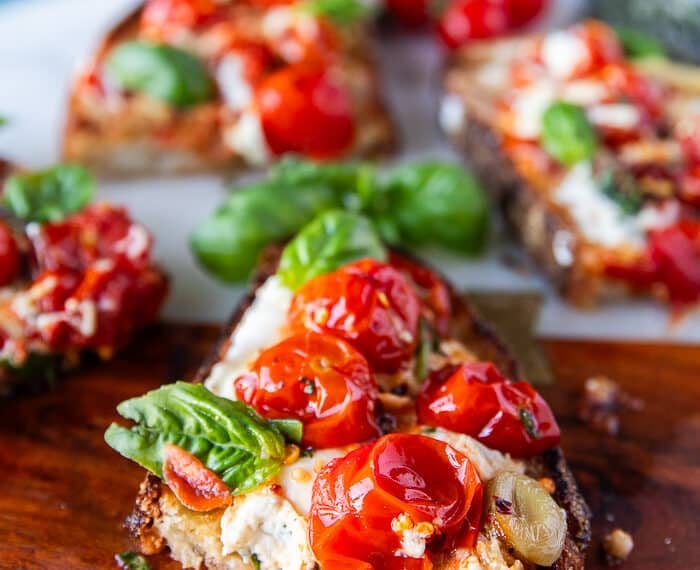 close up of a cut up caprese toast showing the blistered tomatoes, mozzarella and basil leaves drizzled with some olive oil and light balsamic syrup