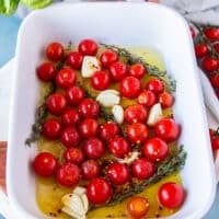 The baby tomatoes, whole crushed garlic cloves, lots of olive oil and fresh thyme are added to a baking dish