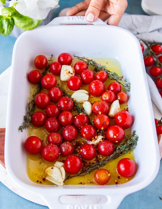 The baby tomatoes, whole crushed garlic cloves, lots of olive oil and fresh thyme are added to a baking dish 