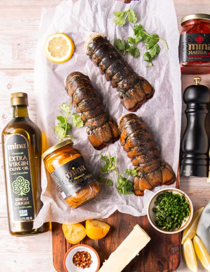 Ingredients to make grilled lobster tail including fresh lobster tails, some preserved lemons, some butter, fresh herbs, some olive oil, salt and pepper 