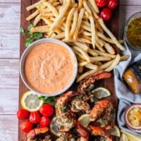 full platter of grilled lobster, fries, some harissa aioli, lemon wedges and baby tomatoes on the side