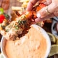 A hand holding grilled lobster dipped in harissa aioli close up showing the texture