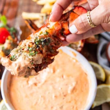 A hand holding grilled lobster dipped in harissa aioli close up showing the texture