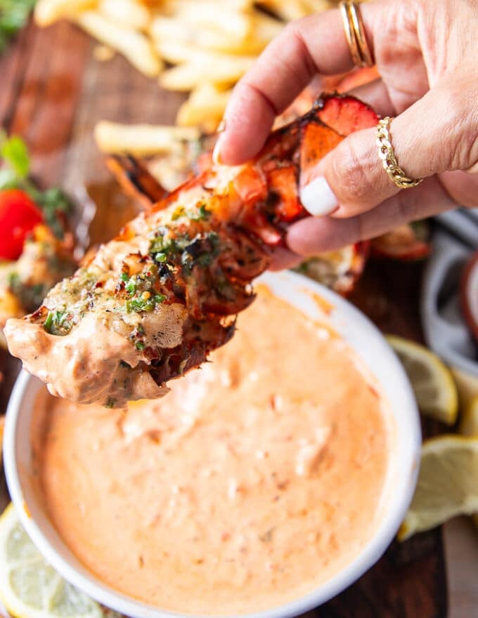 A hand holding grilled lobster dipped in harissa aioli close up showing the texture