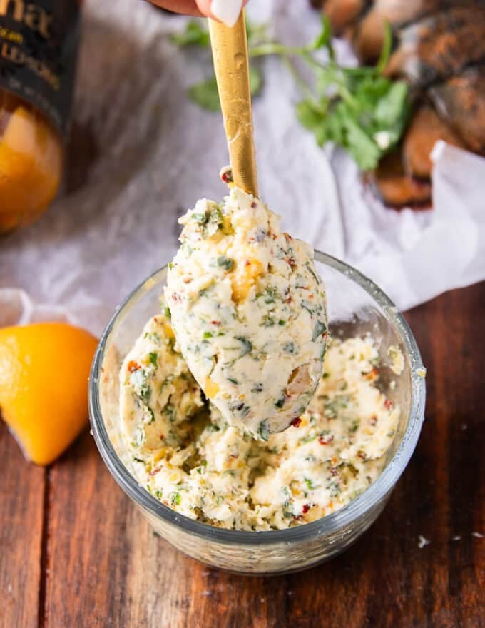 A spoon holding some butter with herbs and preserved lemons with chilli flakes and seasoning. 