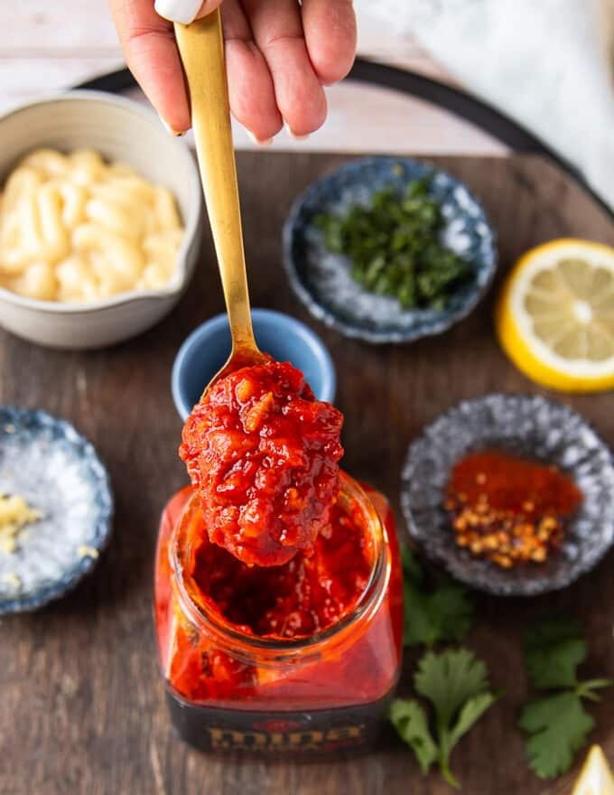 A hand holding a spoonful of harissa paste close up from a jar showing the sauce