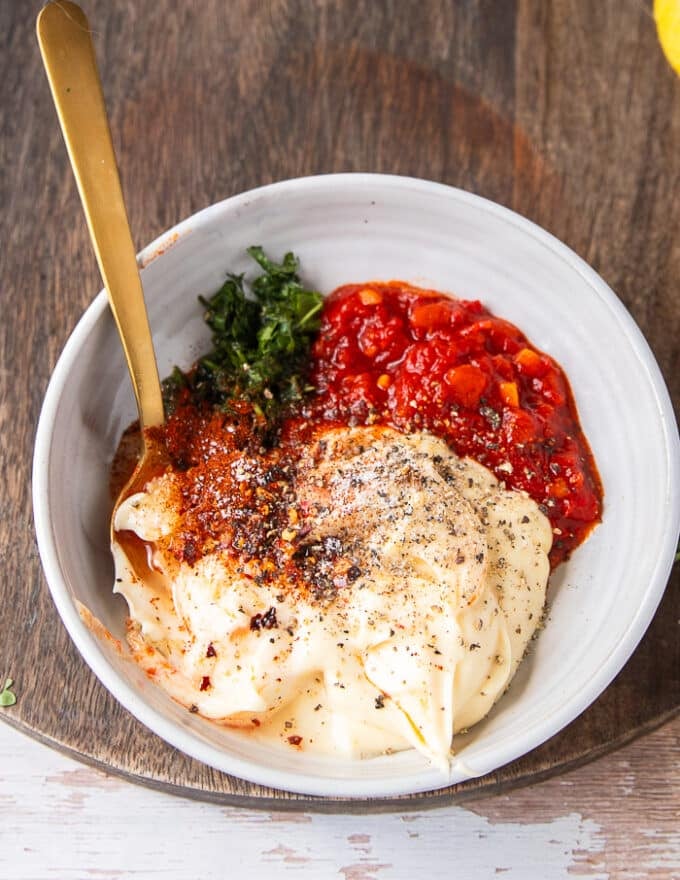 Ingredients to make harissa aioli all added into one bowl and a spoon on the side to mix them up