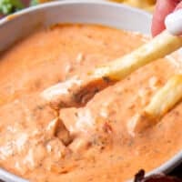 close up of a french fry dipped into harissa aioli and the sauce dripping off the fries