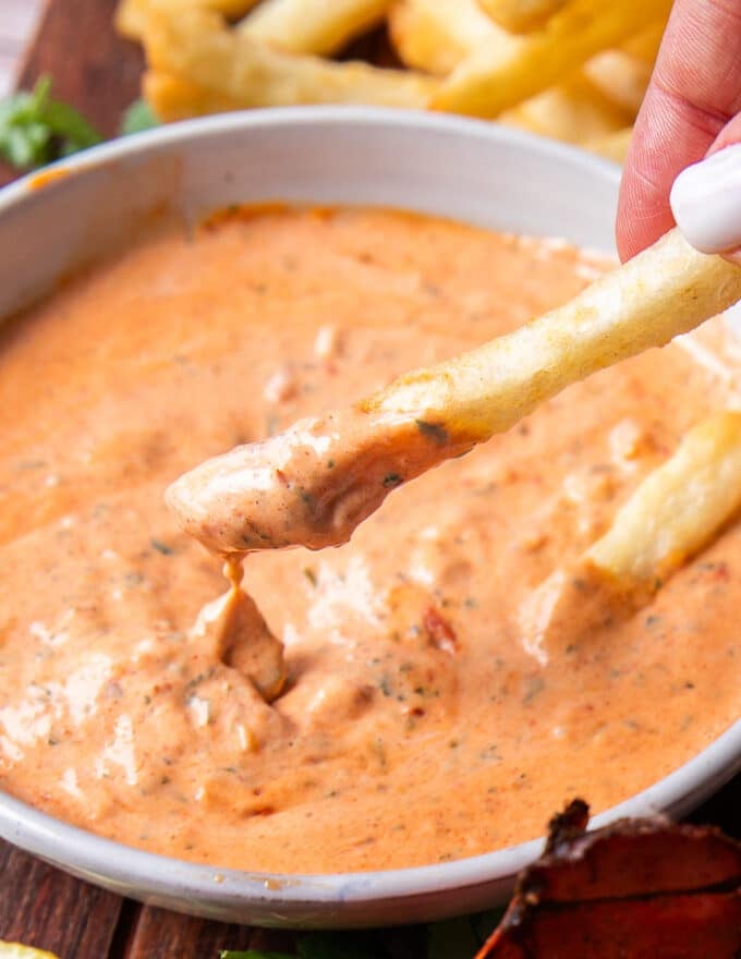close up of a french fry dipped into harissa aioli and the sauce dripping off the fries 
