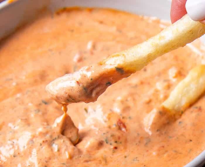 close up of a french fry dipped into harissa aioli and the sauce dripping off the fries