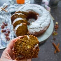 A hand holding a slice of date cake showing the smooth texture and chunky walnuts in the cake with bits of dates showing