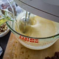 A hand pouring the oil into the bowl of eggs and sugar