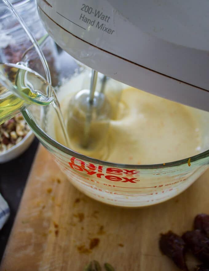 A hand pouring the oil into the bowl of eggs and sugar
