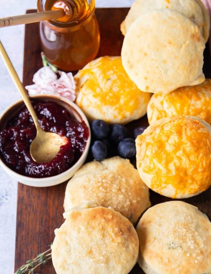A board with fluffy mayonnaise biscuits all over and some jam in a small plate with a spoon on the side 