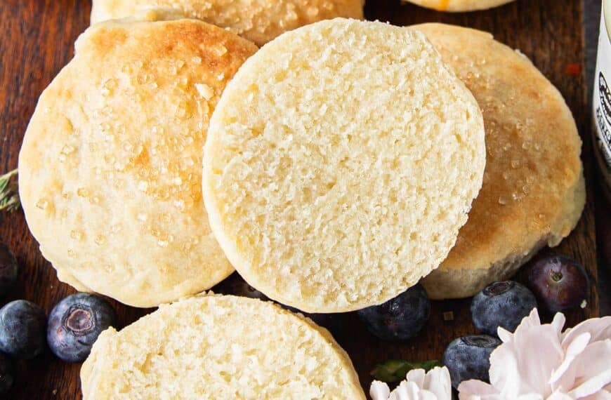 A mayonnaise biscuit split in half showing the fluffy texture on the inside on a plate with other biscuits
