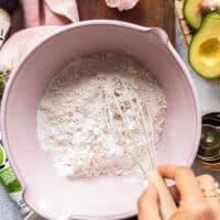 A hand whisking the flour, salt and baking powder in a large bowl to make the dough