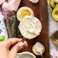 A hand holding a half cup measuring c up with mayonnaise