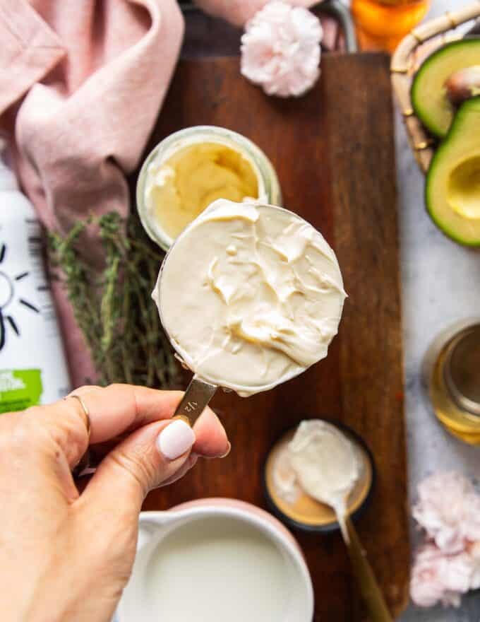 A hand holding a half cup measuring c up with mayonnaise 