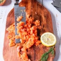 A knife dicing the fresh salmon fillet on a board to make salmon patties