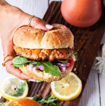 A hand holding salmon burgers assembled and ready
