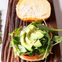 salmon burger toppings added to the bun including onions, tomatoes, avocado and arugula