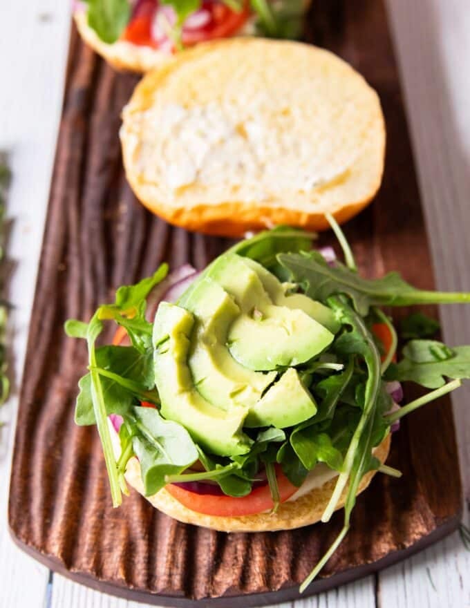 salmon burger toppings added to the bun including onions, tomatoes, avocado and arugula