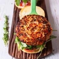 The golden perfectly cooked salmon burger going on to the bun to make the burger somplete