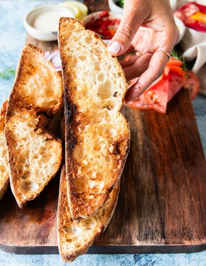 A hand holding toasted crunchy sourdough toasted slices to make sardines on toast 