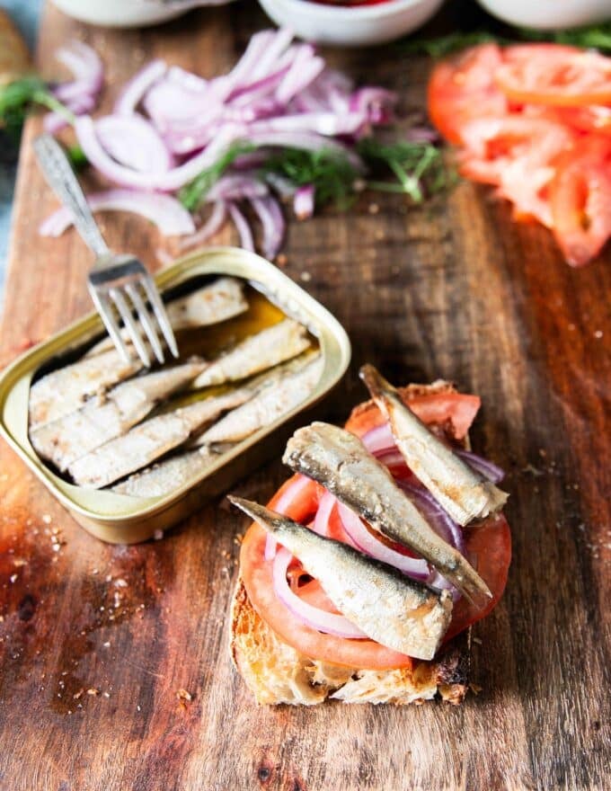 4 pieces of baby sardines from the can are placed over the tomatoes and onions on the toast to layer the toast recipe