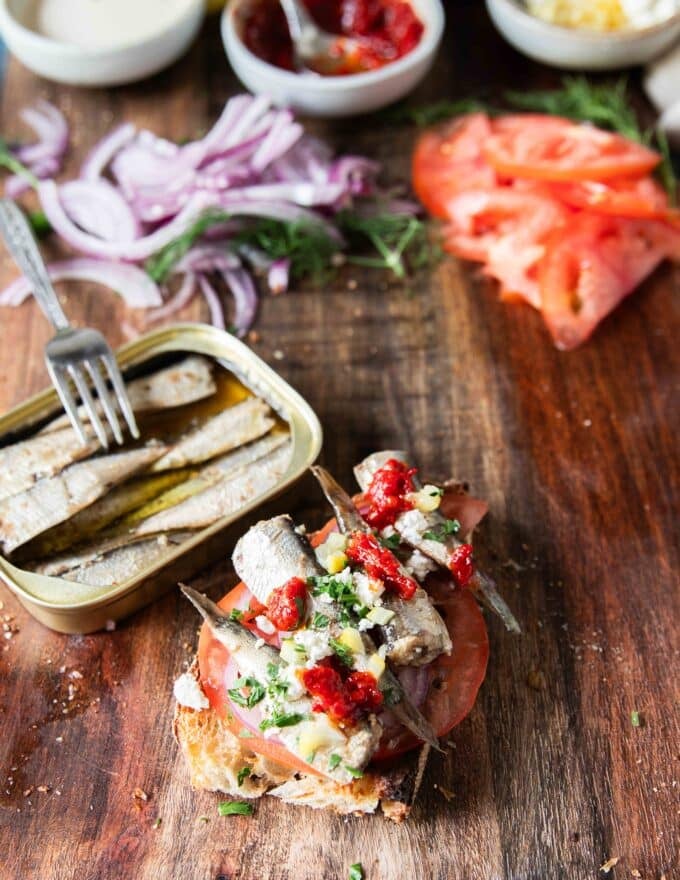 Feta cheese, herbs, hot sauce dollops, preserved lemons or regular lemon, dill are added over the sardines