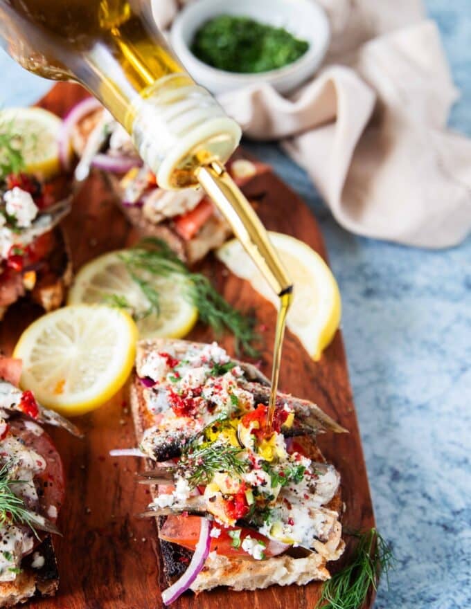 A bottle drizzling some olive oil over the sardines on toast to finish the recipe 