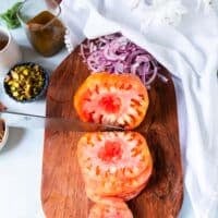 Making the tomato carpaccio recipe: A hand slicing the heirloom tomatoes using a sharp knife on a board