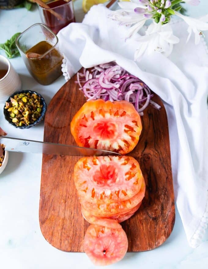 Making the tomato carpaccio recipe: A hand slicing the heirloom tomatoes using a sharp knife on a board