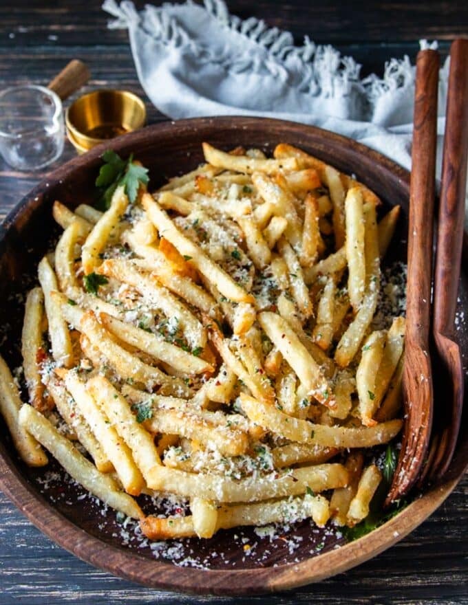 homemade truffle fries close up in a wooden bowl dressed with truffle oil, parmesan cheese, parsley and garlic