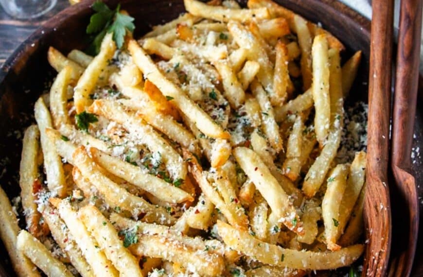 homemade truffle fries close up in a wooden bowl dressed with truffle oil, parmesan cheese, parsley and garlic