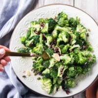 Broccoli salad with creamy dressing on a plate and a hand scooping it
