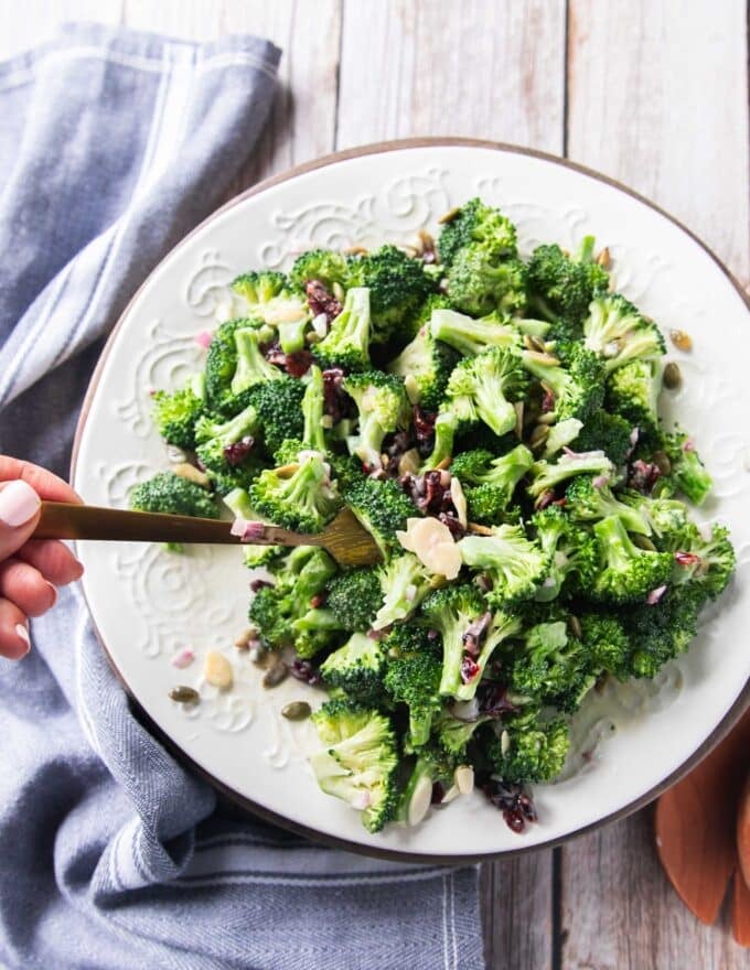 Broccoli salad with creamy dressing on a plate and a hand scooping it 