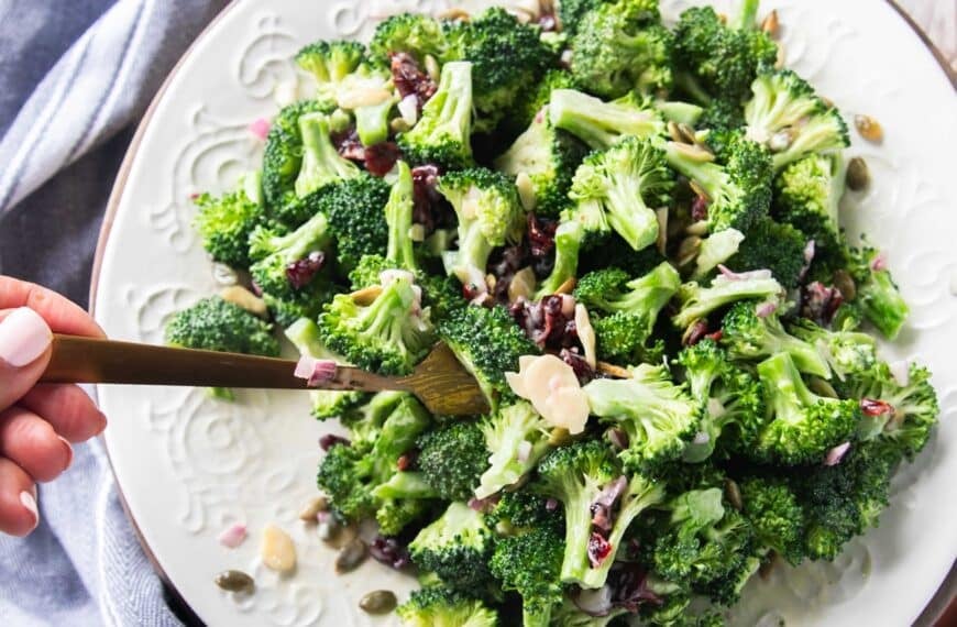 Broccoli salad with creamy dressing on a plate and a hand scooping it